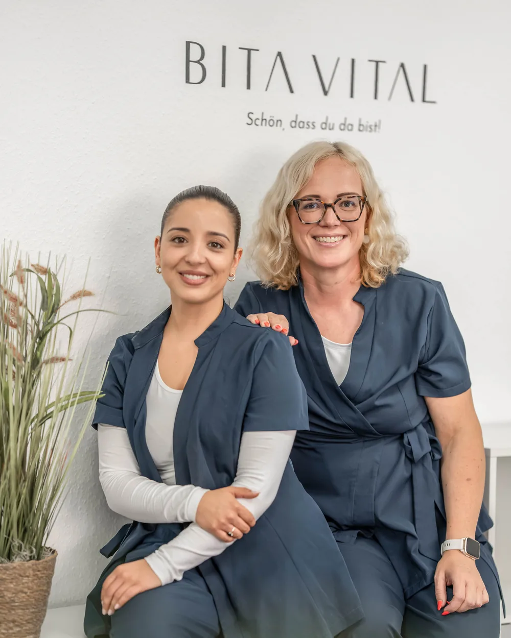 Das Team von BITA VITAL sitzt lächelnd vor dem Logo an der Wand